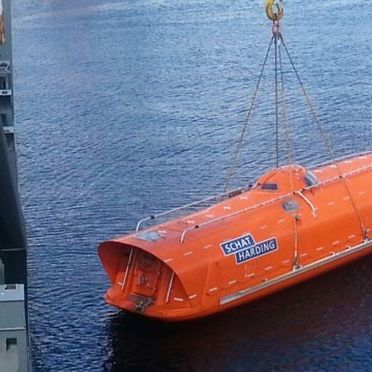 En liten oransje båt som blir senket ned i havet ved hjelp av en kran