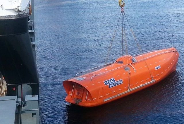 En liten oransje båt som blir senket ned i havet ved hjelp av en kran