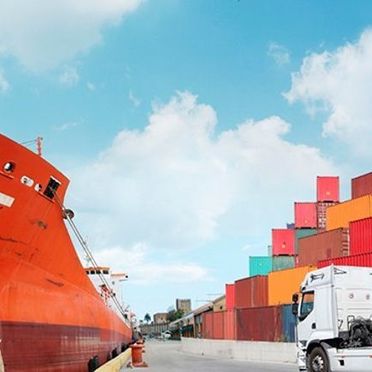 Stort lasteskip som har containere på seg med en lastebil som kjører en grønn container mot skipet