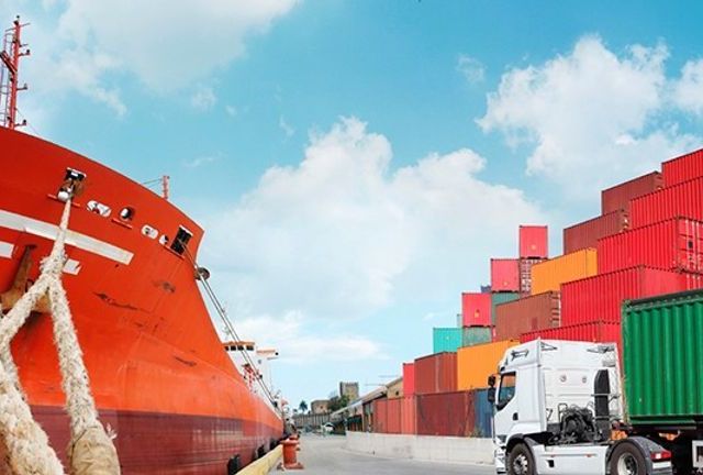 Stort lasteskip som har containere på seg med en lastebil som kjører en grønn container mot skipet